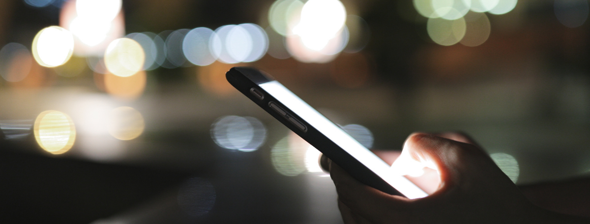 Person using a mobile phone at night with blurred streetlights in background