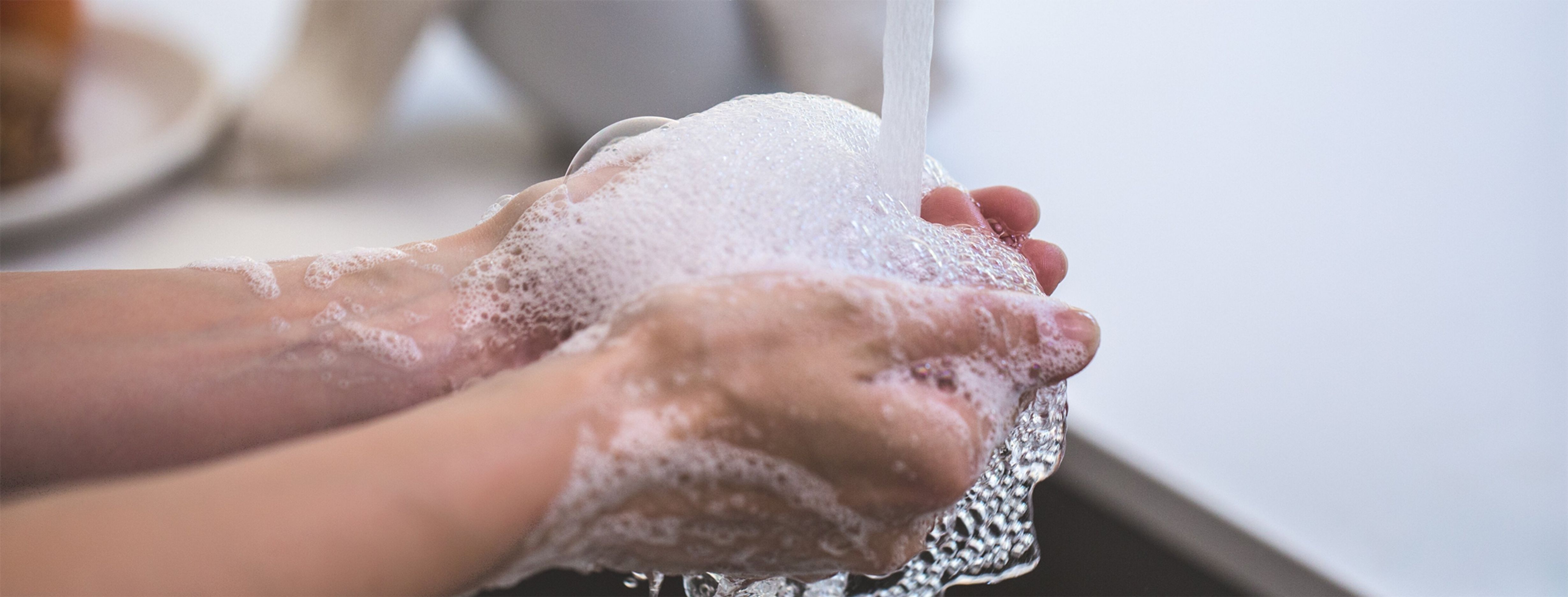A pair of hands being washed with soap under a tap.