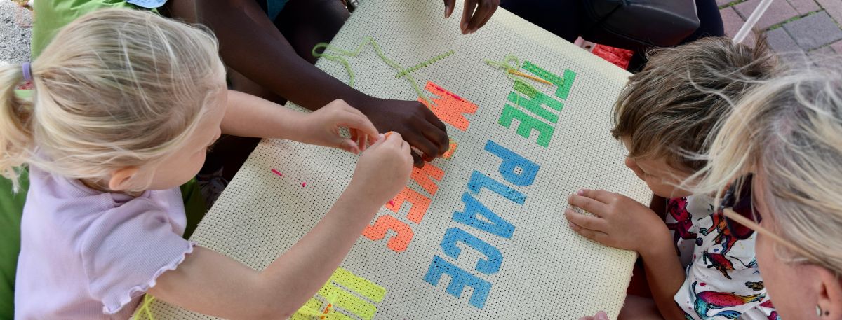 Children sewing a sign that says "the place that makes us"