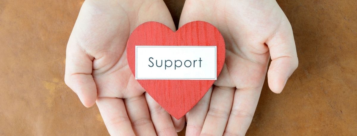 Pair of hands holding a cut out heart shape with the words support on it