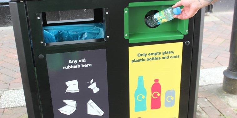 someone putting an empty plastic bottle in the new recycling section of the bins