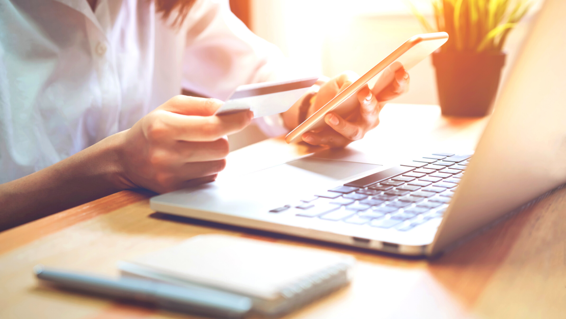 Woman making a payment using her phone, bank card and laptop