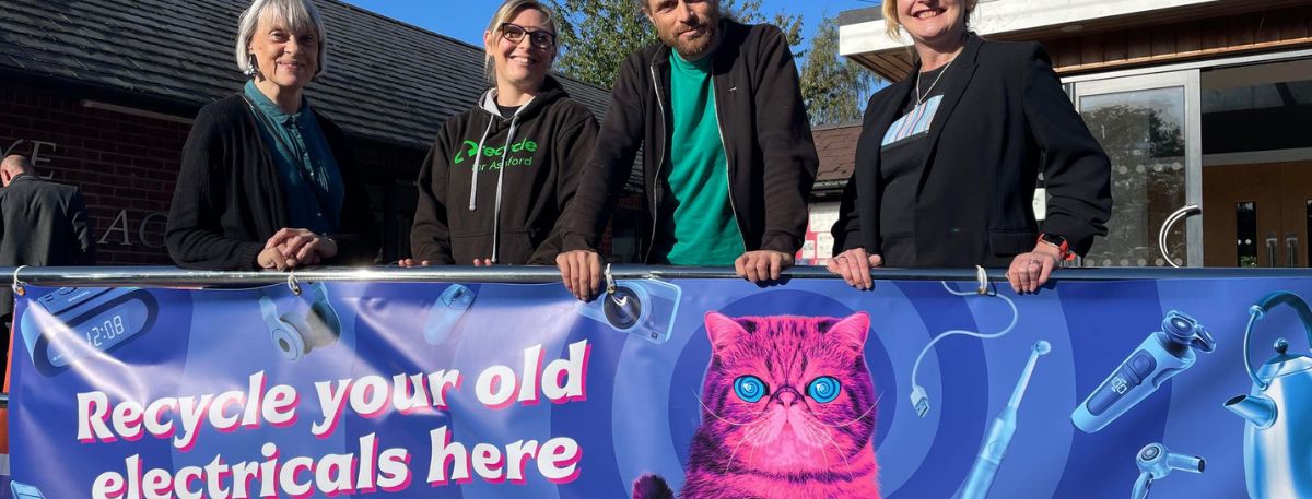 People standing behind banner that says Recycle your old electricals here